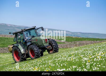 Agriculteur épandant de l'engrais sur un pré de foin traditionnel dans les Yorkshire Dales à l'aide d'un tracteur Hurlimann et d'un épandeur Teagle fert. Yorkshire du Nord, Banque D'Images