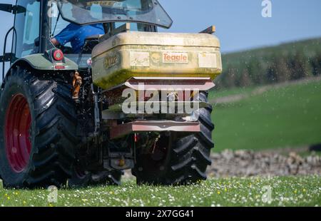 Agriculteur épandant de l'engrais sur un pré de foin traditionnel dans les Yorkshire Dales à l'aide d'un tracteur Hurlimann et d'un épandeur Teagle fert. Yorkshire du Nord, Banque D'Images