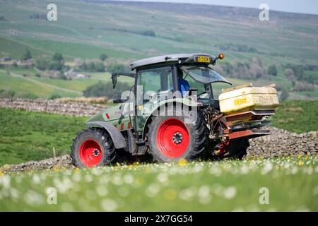 Agriculteur épandant de l'engrais sur un pré de foin traditionnel dans les Yorkshire Dales à l'aide d'un tracteur Hurlimann et d'un épandeur Teagle fert. Yorkshire du Nord, Banque D'Images