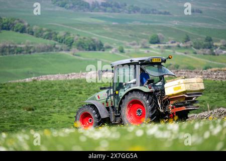 Agriculteur épandant de l'engrais sur un pré de foin traditionnel dans les Yorkshire Dales à l'aide d'un tracteur Hurlimann et d'un épandeur Teagle fert. Yorkshire du Nord, Banque D'Images