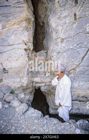 Wadi Bani Kharus, Oman, péninsule arabique, moyen-Orient. Eau du Rocher. Un omanais se rafraîchit avec de l'eau fraîche sortant d'une fente dans le Banque D'Images