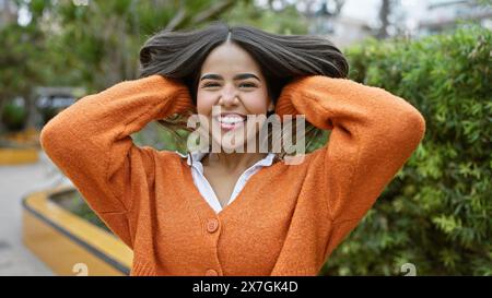 Une jeune femme hispanique joyeuse aime le plein air, son sourire vibrant complétant le cadre verdoyant du parc. Banque D'Images