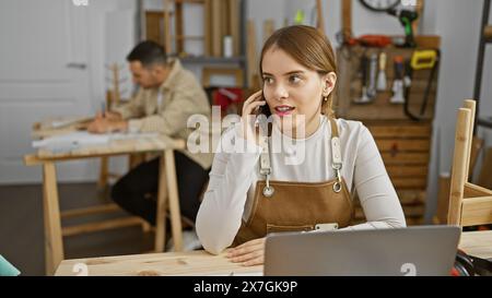 Une femme au téléphone dans un atelier avec un homme dessinant en arrière-plan. Banque D'Images