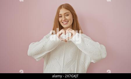 Jeune femme joyeuse formant le cœur avec les mains sur fond rose, exprimant l'amour, la joie et la positivité. Banque D'Images