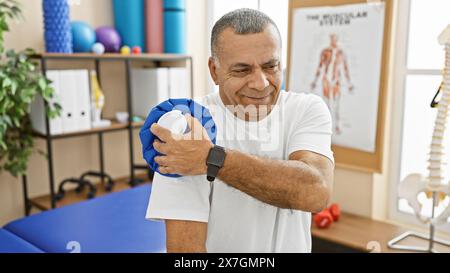 Homme hispanique d'âge moyen appliquant un sac de glace à l'épaule en clinique de physiothérapie. Banque D'Images