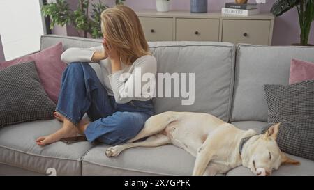 Une jeune femme et un chien reposant sur un canapé dans un salon confortable avec des oreillers décoratifs Banque D'Images