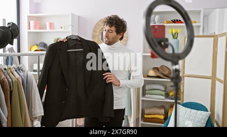 Un beau jeune homme examine une veste dans une salle de vêtements intérieure bien organisée avec divers articles de mode. Banque D'Images