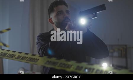 Homme hispanique avec la barbe tenant le pistolet et la lampe de poche sur la scène de crime intérieure Banque D'Images