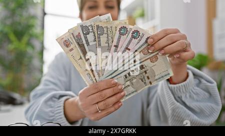 Une jeune femme hispanique affiche des livres égyptiennes dans un bureau bien éclairé. Banque D'Images