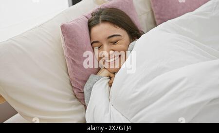 Une jeune femme hispanique souriante profitant de la détente dans une chambre confortable, exsudant bonheur et confort. Banque D'Images
