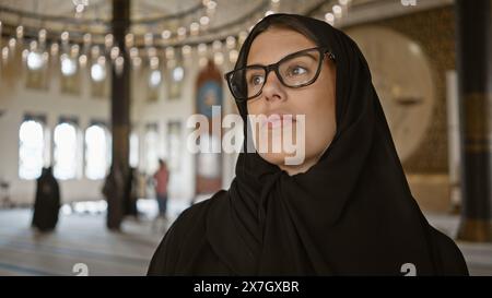 Femme réfléchie en hijab contemplant dans la mosquée qatarienne ornée, incarnant le tourisme culturel et l'architecture islamique Banque D'Images