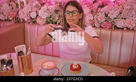 Femme adulte photographiant des desserts dans un café floral rose Banque D'Images