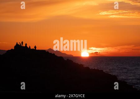Silhouette d'un groupe de personnes sur une colline regardant le coucher du soleil sur la mer Banque D'Images