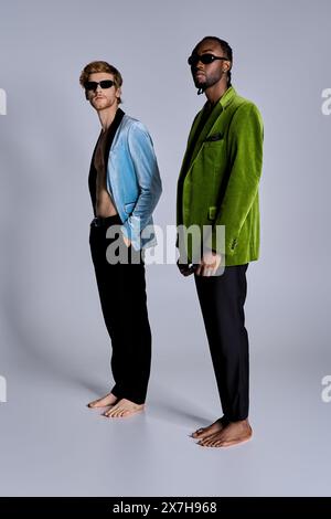 Deux beaux hommes multiculturels dans un style élégant dapper posant ensemble devant un fond gris. Banque D'Images