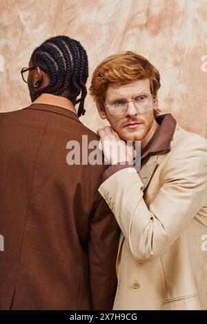 Des hommes multiculturels en lunettes et en trench-coat prennent la pose ensemble. Banque D'Images