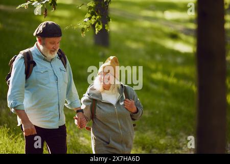 Couple senior, homme souriant et femme randonnant dans un parc luxuriant, portant une tenue confortable décontractée, partageant des aventures en plein air Banque D'Images