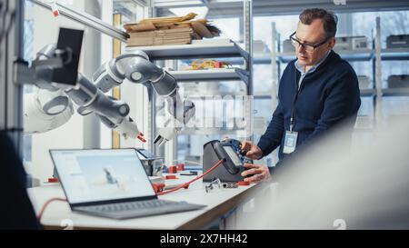 Développeur senior masculin travaille sur un projet d'ingénierie, change la position de la main robotique avec levier. Ingénieur habilité réalisant un projet créatif. Robotique et automatisation pour les installations concept. Banque D'Images