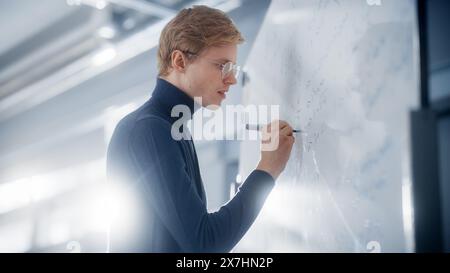 Intelligent Young Academic écrivant une formule mathématique ou une équation grande et complexe sur le tableau blanc. Résolution de problèmes et recherche de nouveaux concepts de stratégies efficaces. Banque D'Images