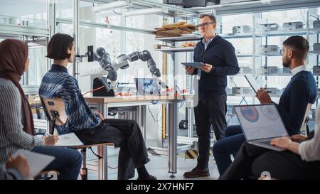 Un ingénieur en chef de sexe masculin organise une réunion avec une présentation pour une équipe de spécialistes en informatique. Il explique Controls of robot Arm à un groupe de jeunes scientifiques. Les étudiants travaillent dans Creative Office. Banque D'Images