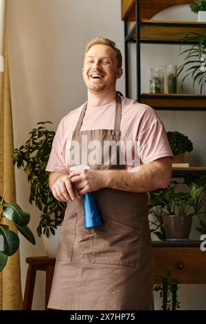 Un homme dans un tablier tient un vaporisateur bleu dans une usine, montrant ses compétences et sa passion pour sa petite entreprise. Banque D'Images