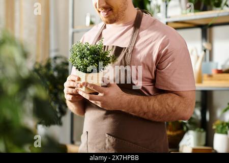 Un homme dans un tablier tient une plante en pot, montrant son amour pour nourrir la vie verte dans son magasin d'usine. Banque D'Images
