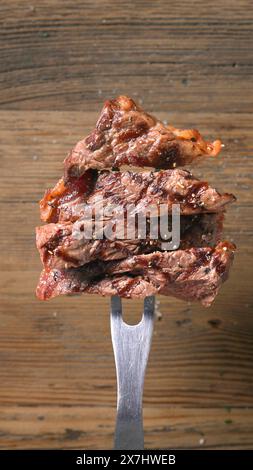 coupes de viande de steak de bœuf fraîchement grillé sur la fourchette sur fond de bois Banque D'Images