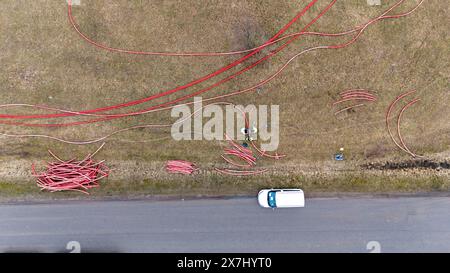 Photographie par drone de travailleurs de la construction, machines industrielles posant un nouveau pipeline près d'une route pendant la journée nuageuse du printemps Banque D'Images