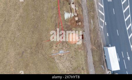 Photographie par drone de travailleurs de la construction, machines industrielles posant un nouveau pipeline près d'une route pendant la journée nuageuse du printemps Banque D'Images