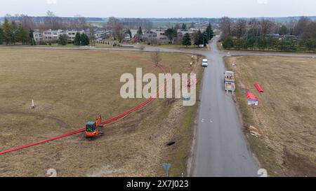 Photographie par drone de travailleurs de la construction, machines industrielles posant un nouveau pipeline près d'une route pendant la journée nuageuse du printemps Banque D'Images