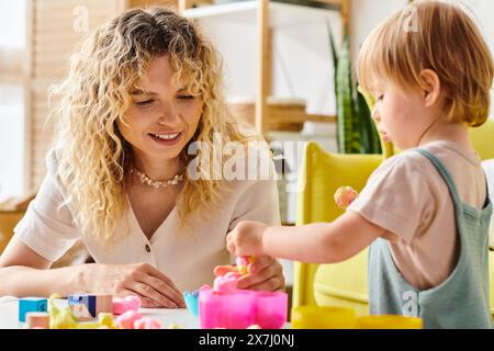 Une mère bouclée et sa fille en bas âge jouent avec joie avec des jouets Montessori à la maison. Banque D'Images