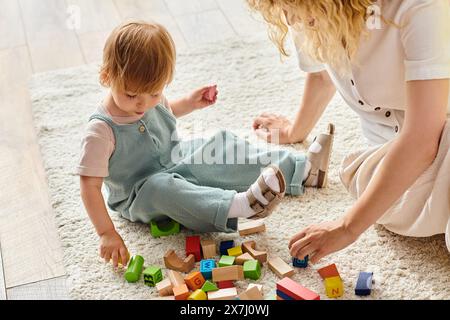 Une mère bouclée s'engage joyeusement avec sa fille en bas âge sur le sol, en utilisant l'éducation Montessori à la maison. Banque D'Images