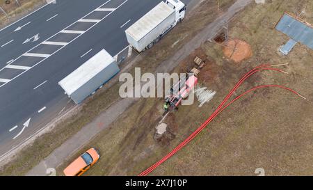 Photographie par drone de travailleurs de la construction, machines industrielles posant un nouveau pipeline près d'une route pendant la journée nuageuse du printemps Banque D'Images