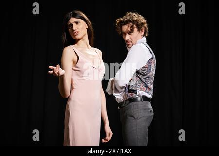 Un homme élégant se tient à côté d'une femme dans une robe rose pendant les répétitions de théâtre. Banque D'Images