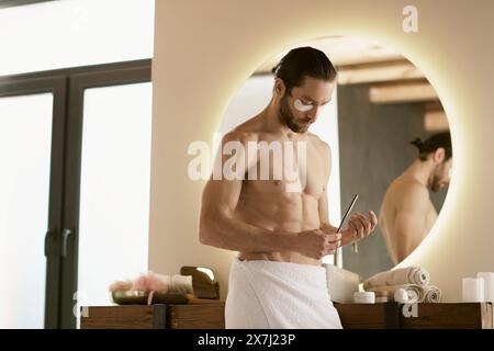 Un homme dans une serviette regarde la lime à ongles tout en faisant sa routine de soins de la peau du matin à la maison. Banque D'Images