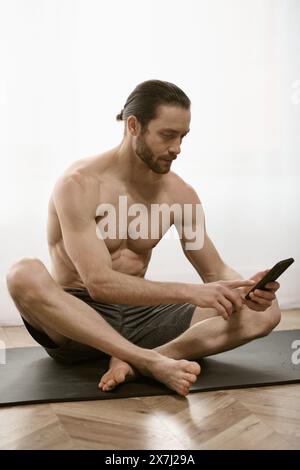 Bel homme, à la maison, fait paisiblement du yoga tout en utilisant un téléphone portable. Banque D'Images