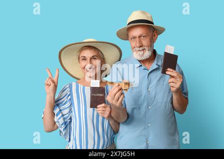 Couple mature avec passeports et avion en bois sur fond bleu. Concept de voyage Banque D'Images