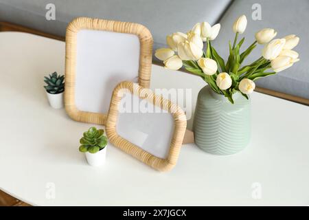 Vase avec tulipes, plantes et cadres photo vierges sur table dans le salon, gros plan Banque D'Images