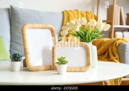 Vase avec tulipes, plantes et cadres photo vierges sur table dans le salon, gros plan Banque D'Images