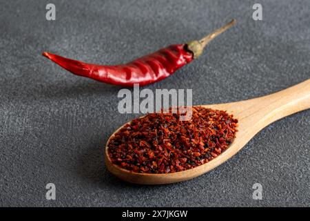 Flocons de poivron rouge. Piments rouges dans une cuillère en bois sur fond noir. Piments secs Banque D'Images