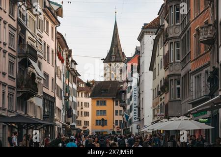 Rue animée de Zurich avec ses clients et ses piétons, la tour de l'horloge de l'église Peter debout haut dans l'horizon Banque D'Images