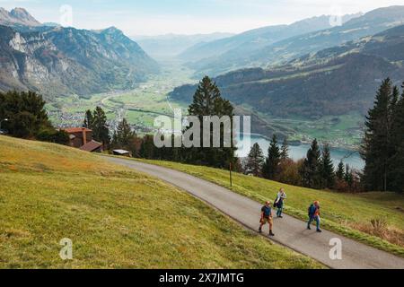 Les randonneurs traversent un chemin pavé serpentant à travers une vallée verdoyante vers la majestueuse chaîne de montagnes Churfirsten en Suisse. Lac Walen vu ci-dessous Banque D'Images