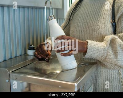 Une jeune femme remplissant sa bouteille réutilisable dans une fontaine d'aéroport Banque D'Images