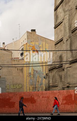 Une murale fantaisiste anime le paysage urbain silencieux de Saragosse, contrastant avec les murs Unis, tandis que deux personnes dans des directions opposées s'approchent l'une de l'autre. Banque D'Images