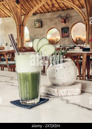 Smoothie vert au concombre dans un verre avec une paille en métal sur une table en marbre en gros plan Banque D'Images