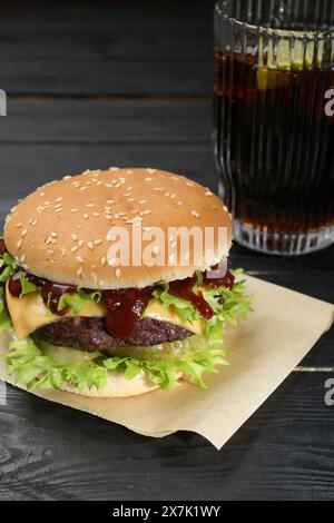 Hamburger avec délicieuse patty et boisson gazeuse sur la table en bois noir Banque D'Images