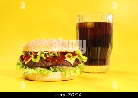 Hamburger avec délicieuse patty et boisson gazeuse sur fond jaune Banque D'Images