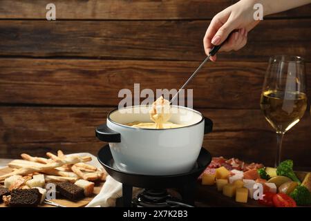 Femme trempant un morceau de pain dans un pot à fondue avec du fromage fondu à table avec des collations, gros plan Banque D'Images