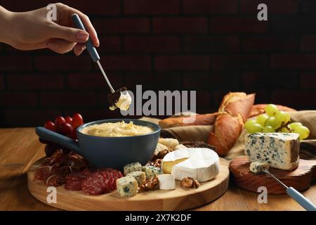 Femme trempant un morceau de pain dans un pot à fondue avec du fromage fondu à la table en bois, gros plan Banque D'Images