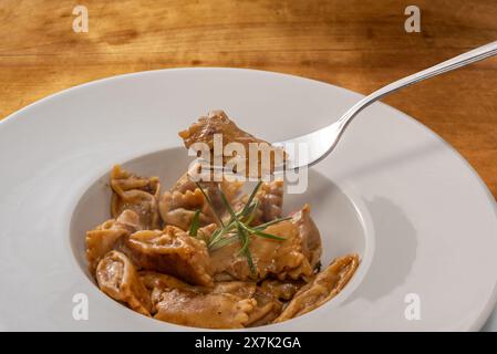 Agnolotti del Plin servi avec sauce rôtie, raviolis de pâtes aux œufs Plin sur fourchette sur assiette blanche sur table en bois Banque D'Images