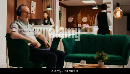 Personne retraitée regarde un film sur ordinateur portable en utilisant des services de streaming en ligne, passant le temps pendant qu'il attend de voir un logement. Le vieux voyageur aime les films sur ordinateur personnel dans le hall. Banque D'Images